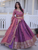 Woman in a traditional purple and pink lehenga with gold embroidery standing on a balcony.