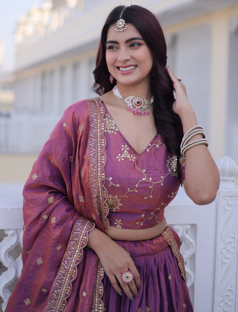 Woman in a traditional purple outfit with gold embroidery, smiling outdoors.