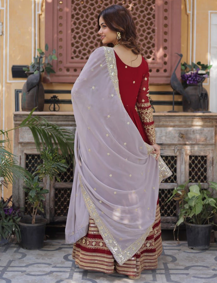 Woman in a red and gold traditional outfit with a light purple saree in an indoor setting.