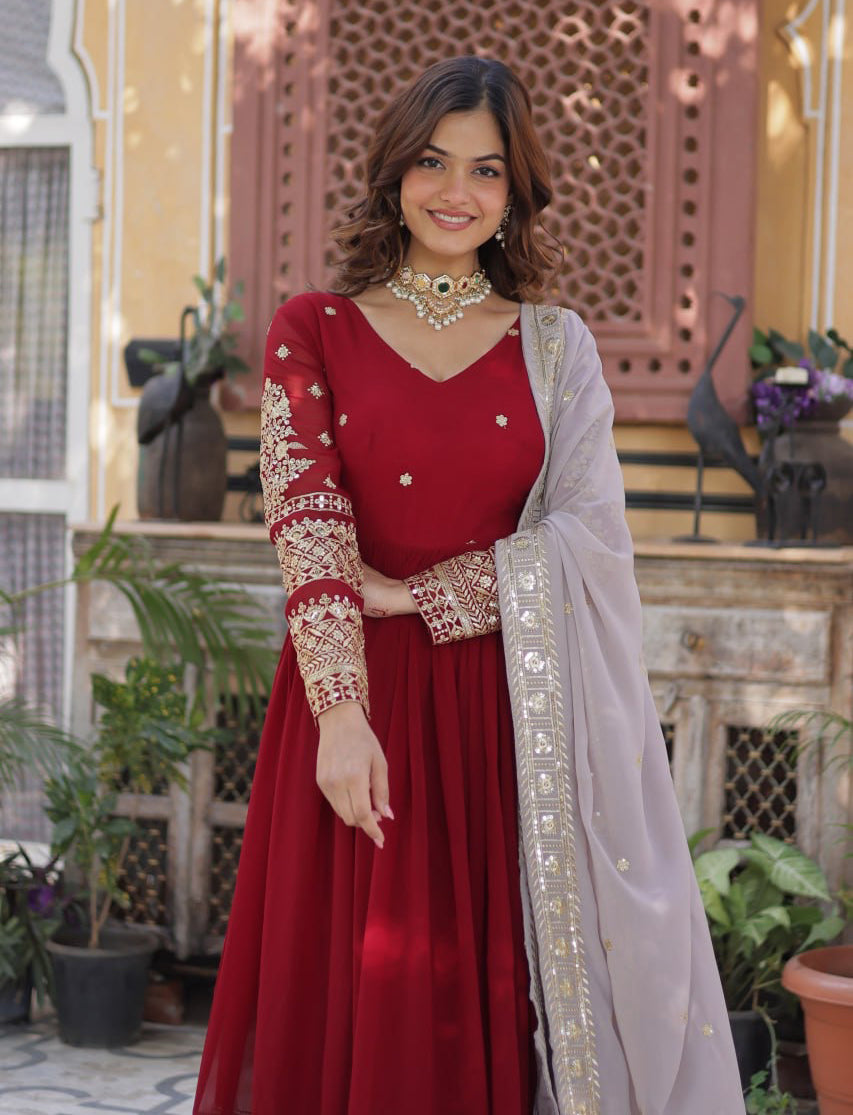 Woman in a red traditional outfit with white embroidery standing outdoors.
