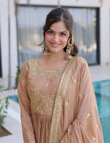Woman wearing a beige embroidered traditional outfit with gold details, standing outdoors.