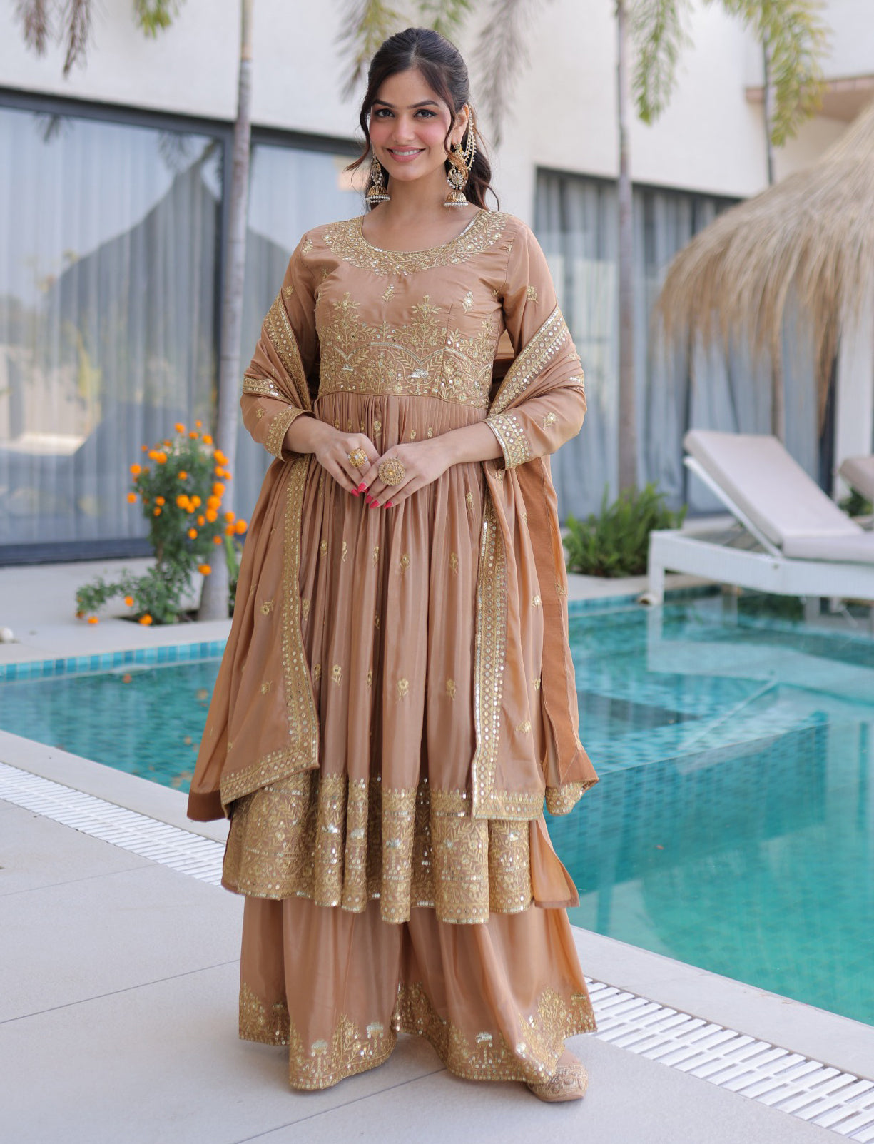 Woman in a beige and gold traditional outfit standing by a poolside.