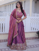 Woman in a traditional purple and pink saree standing in front of a white building.