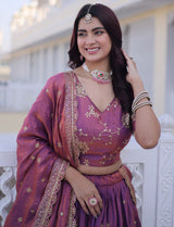 Woman in a traditional purple outfit with gold embroidery, smiling outdoors.