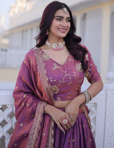 Woman in a traditional purple saree with gold embroidery, smiling outdoors.