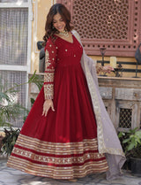 Woman in a red traditional outfit with gold embroidery standing in an outdoor setting.
