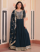 Woman wearing a dark blue traditional outfit with gold embroidery in a decorated room.