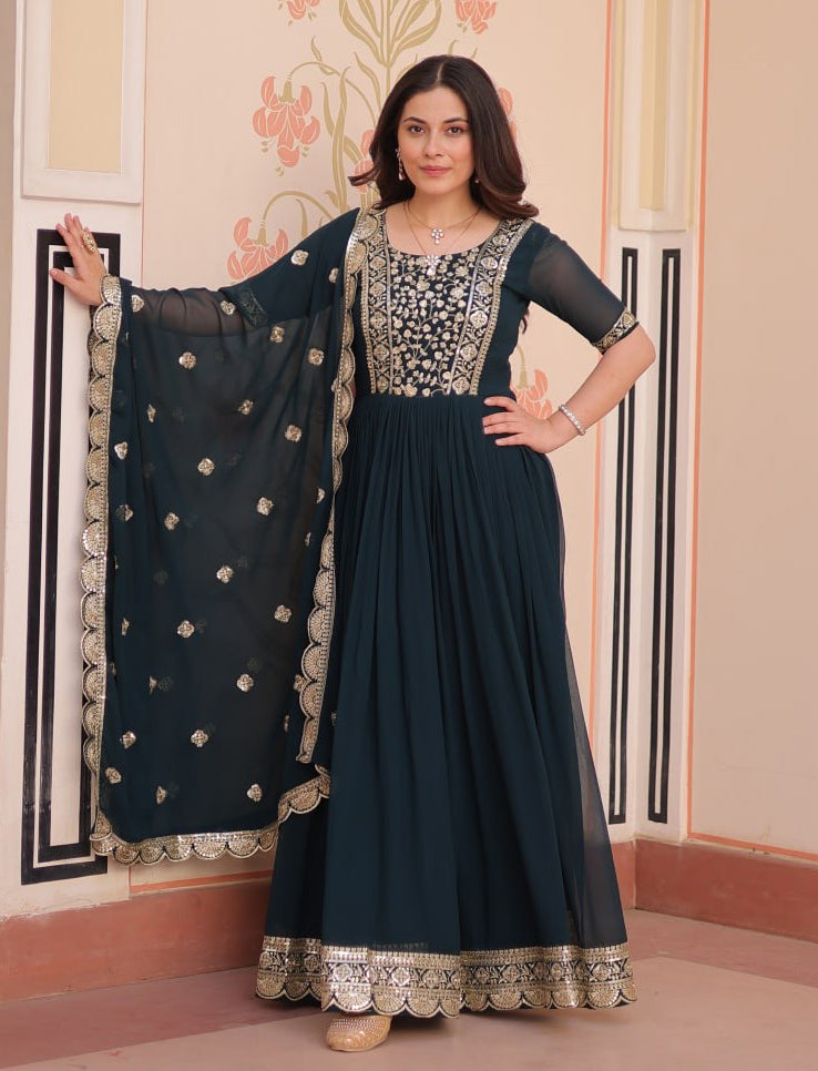 Woman wearing a dark blue traditional outfit with a matching dupatta in a decorated room.