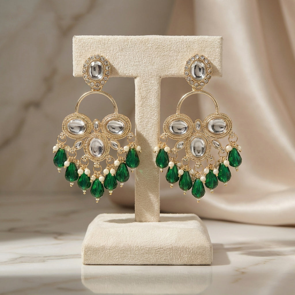 Ornate earrings with green gemstones on a beige stand against a neutral background