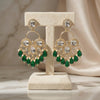 Ornate earrings with green gemstones on a beige stand against a neutral background