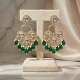 Ornate earrings with green gemstones on a beige stand against a neutral background