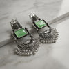 Ornate silver earrings with green stones on a marble surface
