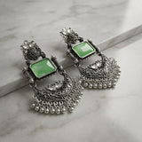 Ornate silver earrings with green stones on a marble surface