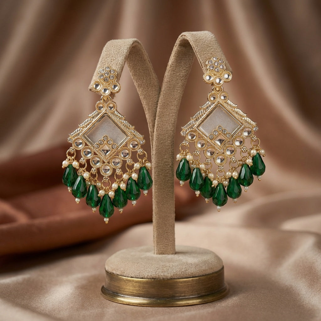 Pair of gold and green earrings on a beige stand against a brown fabric background