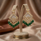 Pair of gold and green earrings on a beige stand against a brown fabric background