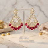 Gold and red earrings on a stand with a marble background