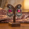 Ornate earrings with pink gemstones on a wooden stand against a blurred background