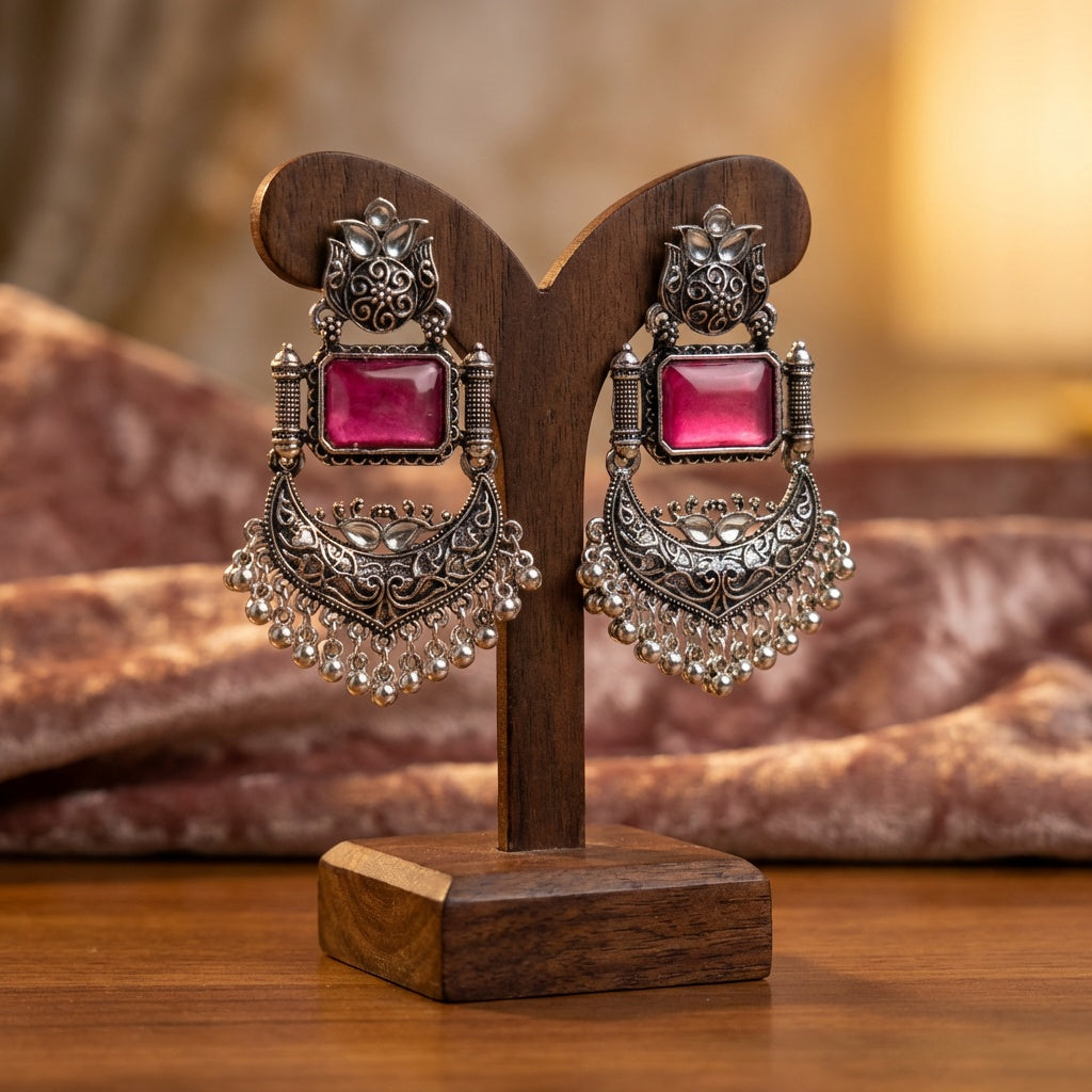 Ornate earrings with pink gemstones on a wooden stand against a blurred background
