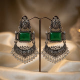 Ornate earrings with green gemstones on a stand against a soft background