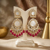 Ornate earrings with red gemstones on a white stand against a warm-toned background