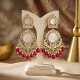 Ornate earrings with red gemstones on a white stand against a warm-toned background