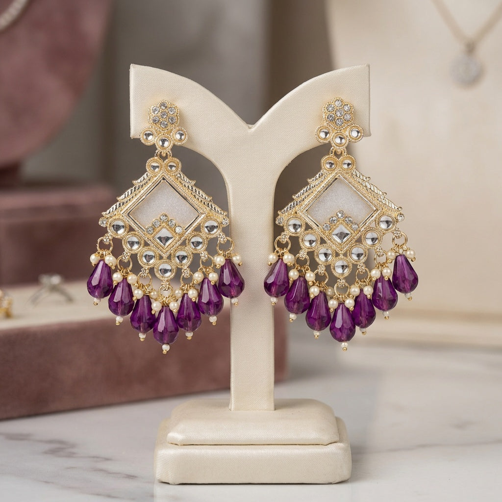 Gold and purple earrings on a white stand with a blurred background