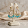 Gold and turquoise earrings on a display stand with a soft background