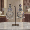 Ornate silver earrings with purple stones on a stand against a blurred background