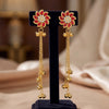 Gold earrings with red floral designs on a black stand against a blurred background