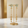 Gold earrings with turquoise stones on a gold stand against a beige background