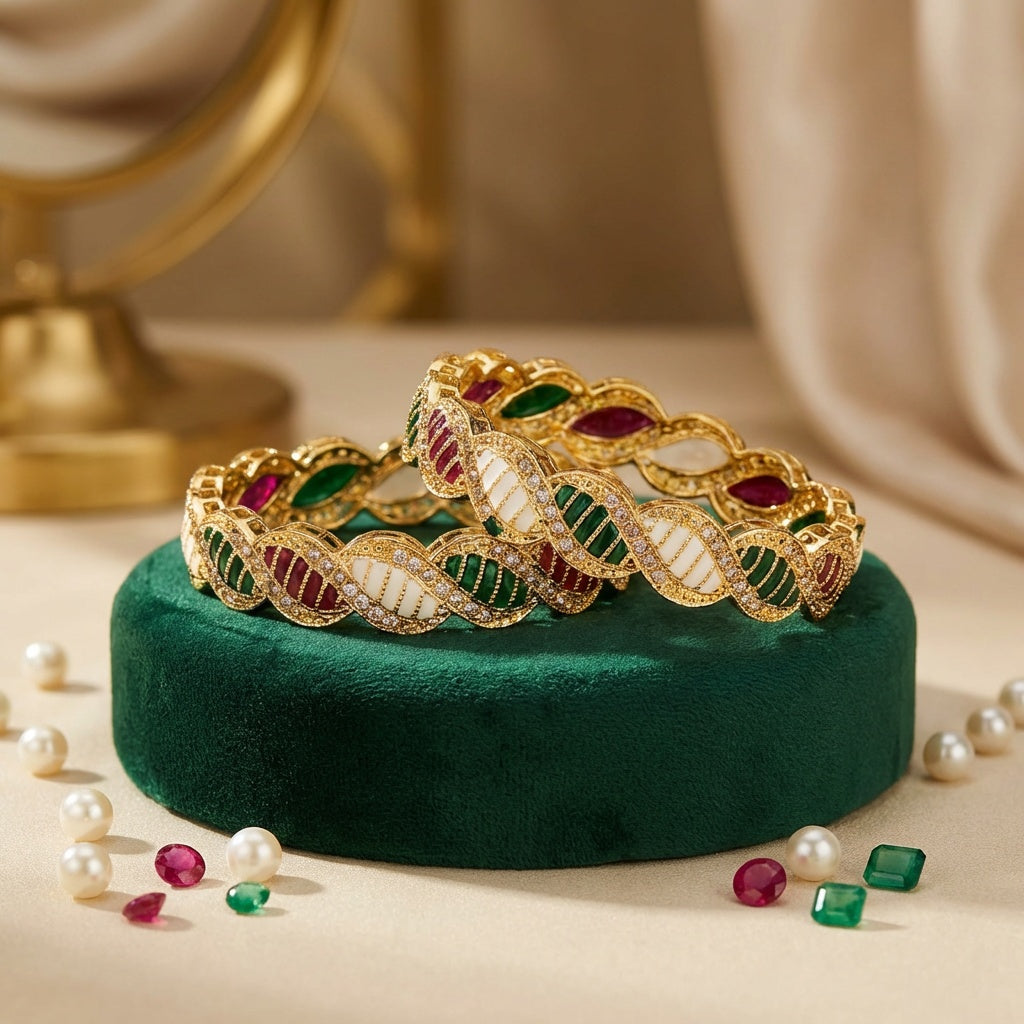 Gold bracelets with gemstones on a green cushion, surrounded by pearls and gemstones.