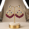Ornate earrings with red beads on a gold stand against a neutral background