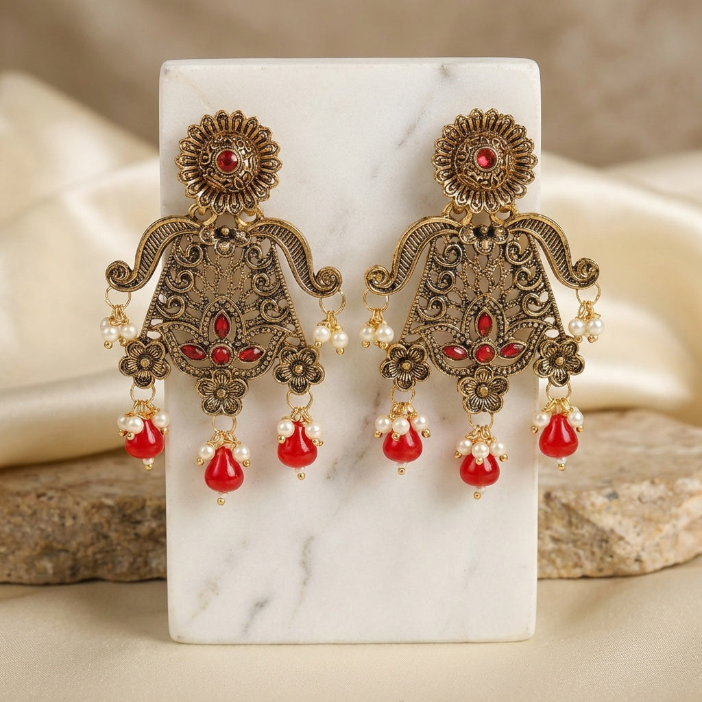 Ornate earrings with red and pearl details on a marble stand.