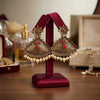 Ornate earrings with red stones and pearls on a red stand against a blurred background