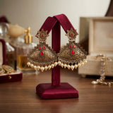 Ornate earrings with red stones and pearls on a red stand against a blurred background