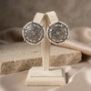 Pair of ornate earrings on a beige stand with a neutral background