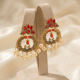 Ornate earrings with red gemstones and pearl drops on a beige stand against a soft beige background