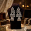 Pair of silver earrings on a black velvet stand with a warm, blurred background.