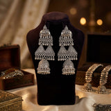 Pair of silver earrings on a black velvet stand with a warm, blurred background.