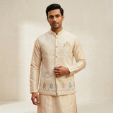 Man wearing a cream-colored traditional outfit with intricate patterns on a plain background