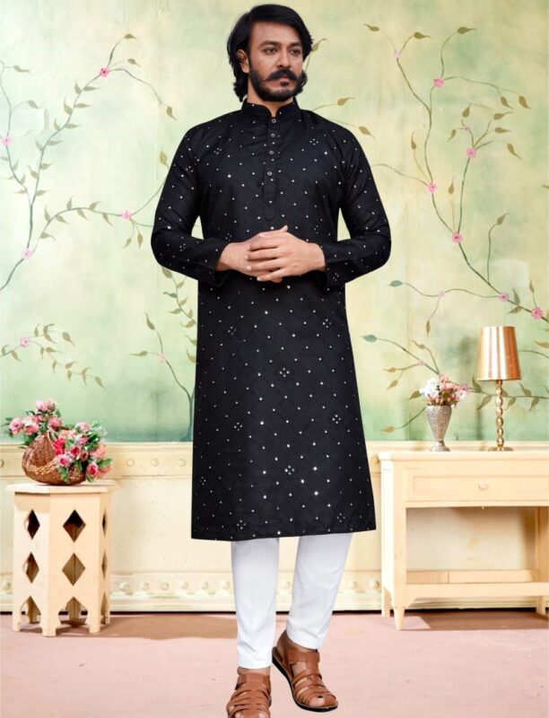 A man elegantly dressed in a black embroidered Kurta for men paired with white pajama and brown sandals.